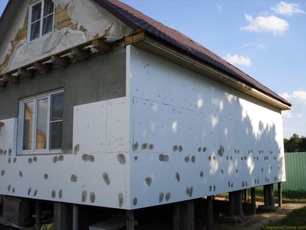 Wooden house insulated with foam boards. Cement mortar covers on the caps of the plastic dowels that hold the material