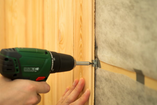 In the photo we see an example of installing plastic wall panels under a tree on a pre-prepared crate, using self-tapping screws and a screwdriver