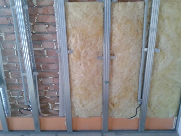 The photo shows the insulation and cladding of a brick wall with drywall using the construction of a metal profile