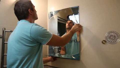 We see the process of mounting a mirror without a frame on the bathroom wall.