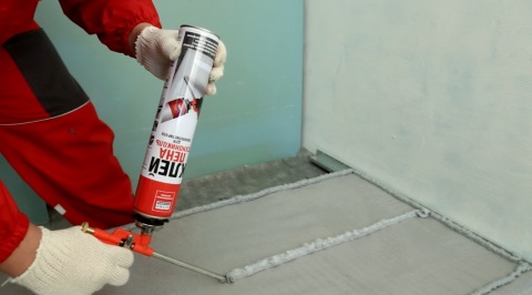 We see the process of applying glue to a foam sheet, for its further installation on the wall